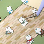 Placing a character sticker onto the Bookshop scene card with tweezers