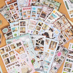 Cat Journey sticker sheets arranged in a flat lay with Japanese-style cat illustrations, room scenes, speech bubbles, plants, and photo-frame details