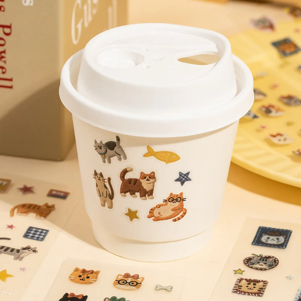 Cat stickers used to decorate a paper cup with fish, stars, and playful cat designs