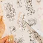 Hand holding assorted celestial and floral journaling sticker sheets from the two designs