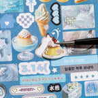 Close-up of a blue dessert sticker sheet showing a pudding sticker being peeled from the page