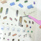 Close-up of a pre-cut window sticker piece being lifted with tweezers from the Cozy Room Stories scene sticker kit