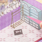 Close-up of a craft rack sticker being placed onto the Dreamy Craft Shop scene card with tweezers