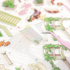 Die-cut Eden Garden sticker piece being lifted from a transparent PVC sticker sheet with tweezers