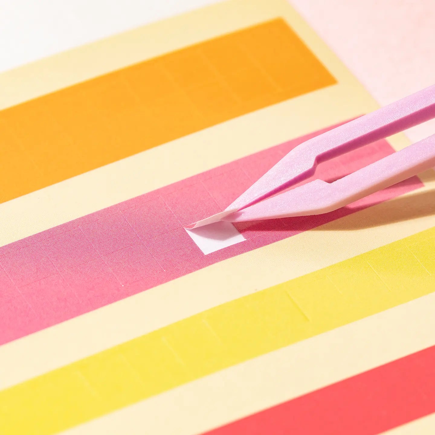Placing a small square sticker onto a numbered pixel mosaic card with tweezers