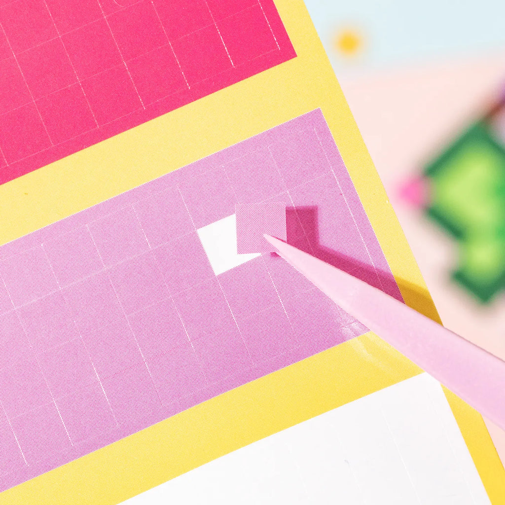 Close-up of a small square sticker block being placed with tweezers