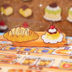Close-up of bread and pudding PET stickers displayed on a bakery scene card