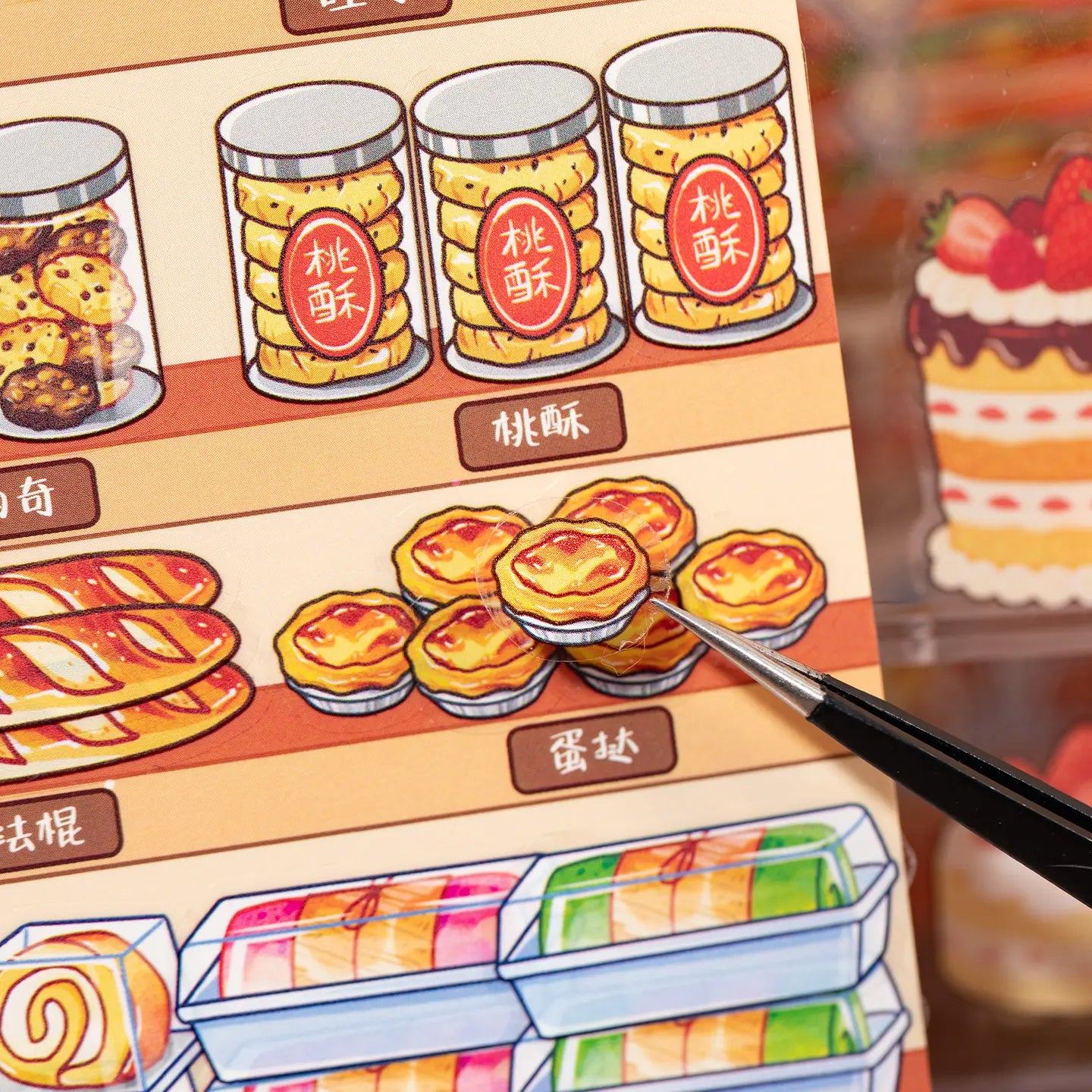 Close-up of an egg tart PET sticker being placed on a bakery scene card