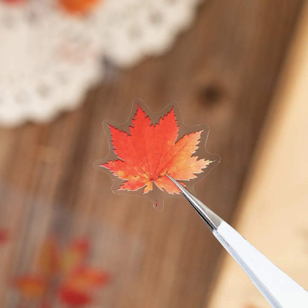 Close-up of an orange maple leaf sticker held with tweezers