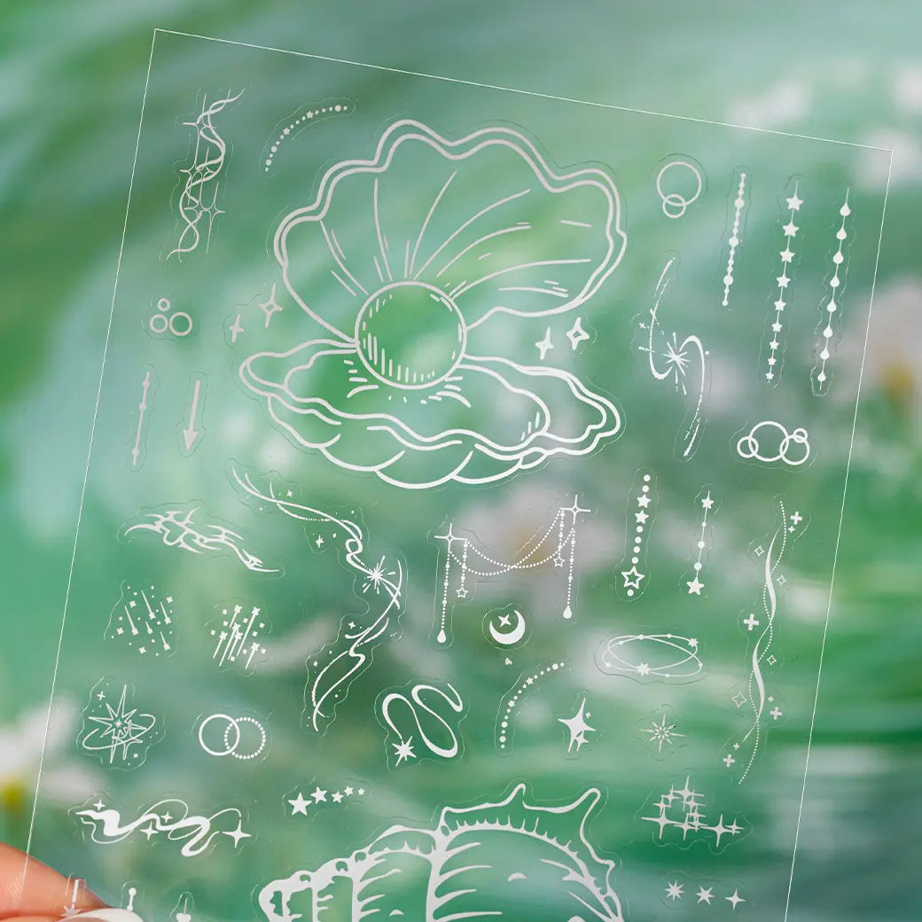 Close-up of a clear PET sticker sheet with white shell, star, moon, and ocean-inspired accent designs