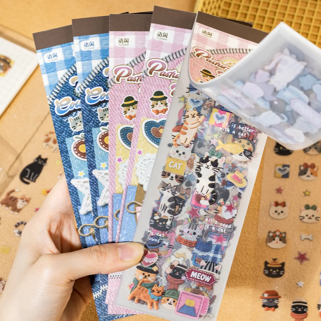 Hand holding the Patchwork Cat Journaling Sticker Set with two packaged styles and loose cat stickers