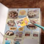 Close-up of a retro milk tea sticker being lifted from the sticker sheet with tweezers