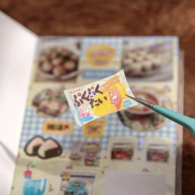 Close-up of a retro milk tea sticker being lifted from the sticker sheet with tweezers