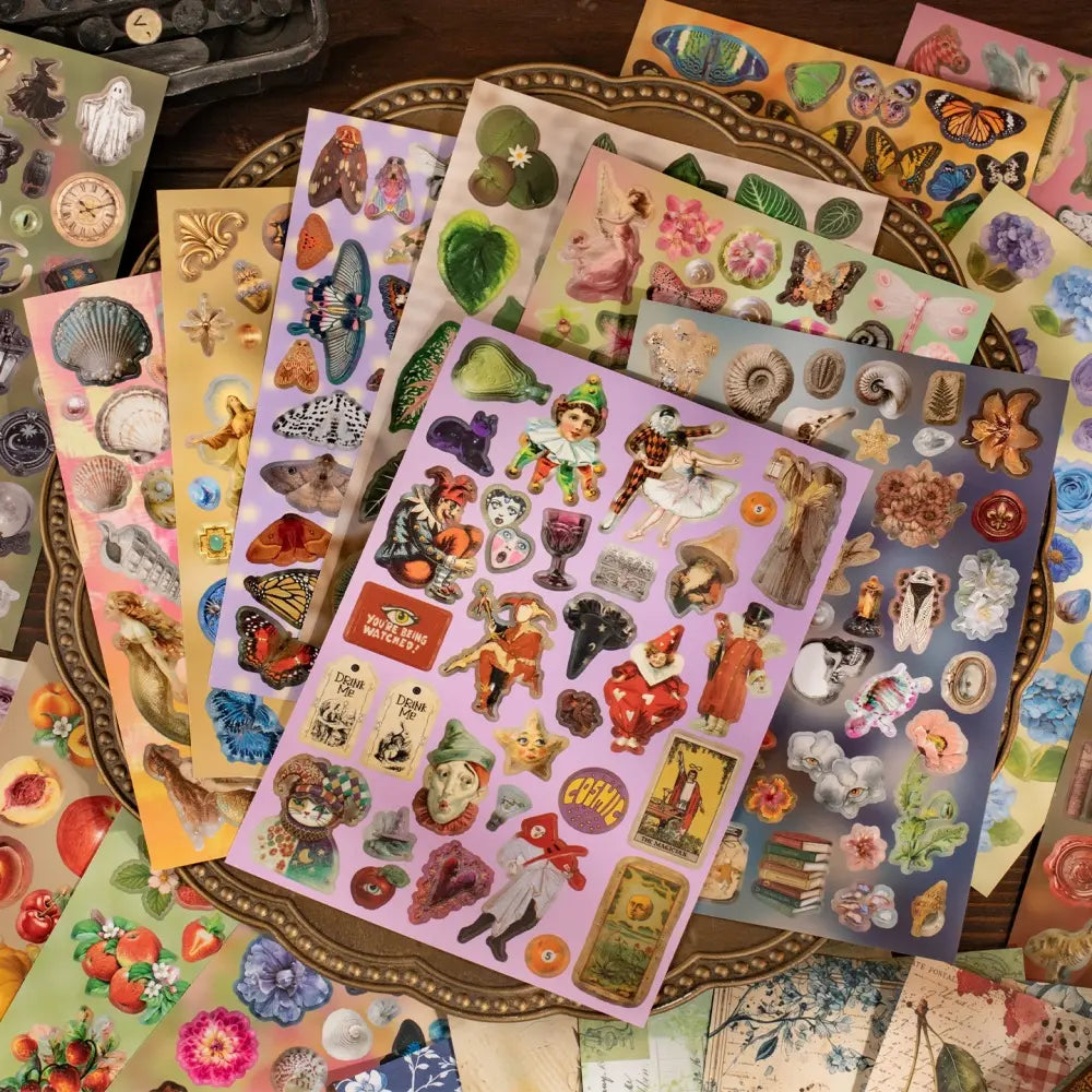 Flat lay of vintage journaling sticker sheets with butterflies, shells, flowers, fruit, and antique-style designs