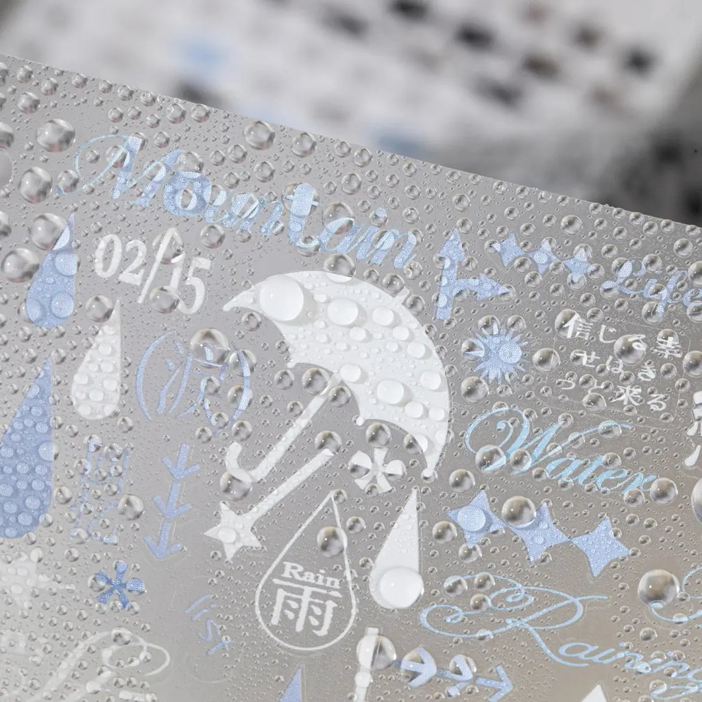 Close-up of a matte transparent Strong Valley sticker sheet with rain and umbrella designs shown with water droplets on the surface