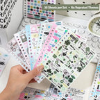 Hand holding several Strong Valley journaling sticker sheets with binder holes, pastel icons, text stickers, labels, arrows, and clover accents
