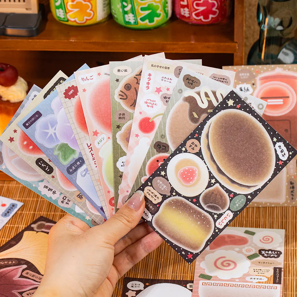 Assorted Tasty Time journaling sticker sheets held in one hand with desserts, fruit, drinks, and food designs