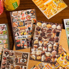 Close-up of Warm Sweet Treats dessert sticker sheets with cakes, chocolate, sushi-style sweets, pastries, and orange dessert designs