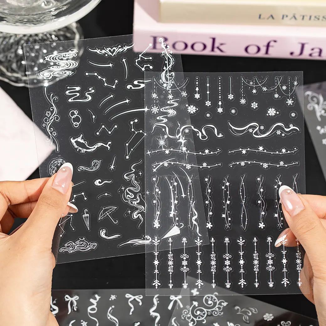 Hands holding clear PET journaling sticker sheets with white stars, borders, music notes, and decorative line designs