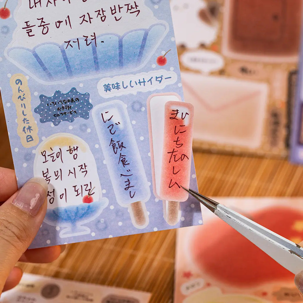 Writable popsicle-shaped paper sticker being lifted from a blue journaling sticker sheet